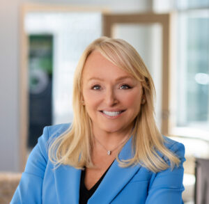 A woman in a blue blazer smiles at the camera during her podcast series.